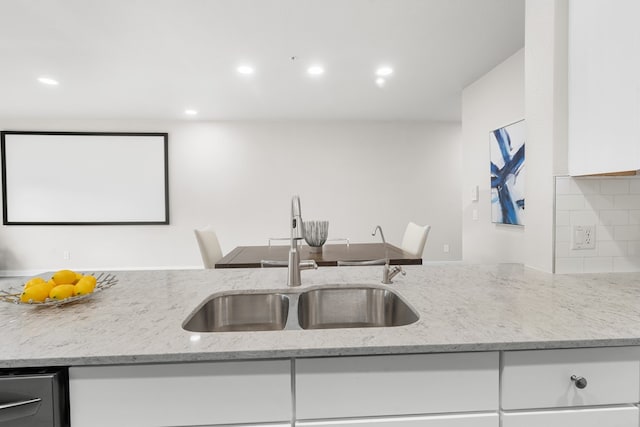 kitchen with decorative backsplash, sink, white cabinets, and light stone counters