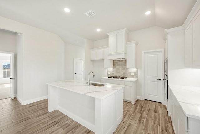 kitchen featuring appliances with stainless steel finishes, an island with sink, sink, white cabinets, and light stone countertops