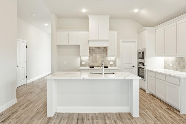 kitchen featuring light stone counters, stainless steel appliances, white cabinets, and a center island with sink