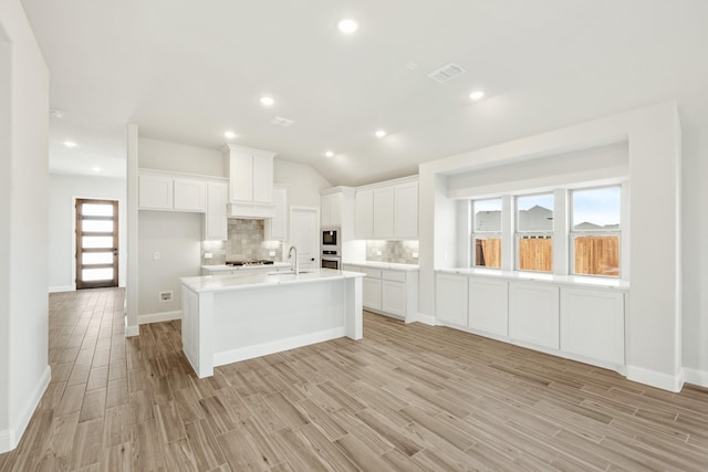 kitchen with light hardwood / wood-style flooring, white cabinets, and a center island with sink