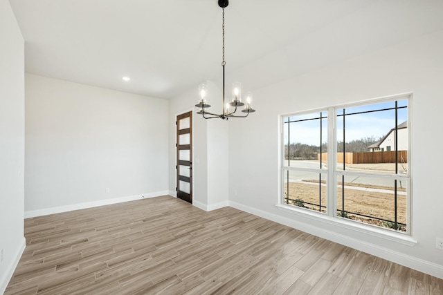 spare room featuring plenty of natural light, a notable chandelier, and light hardwood / wood-style flooring