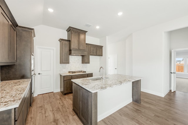 kitchen with vaulted ceiling, stainless steel gas stovetop, an island with sink, sink, and light stone countertops