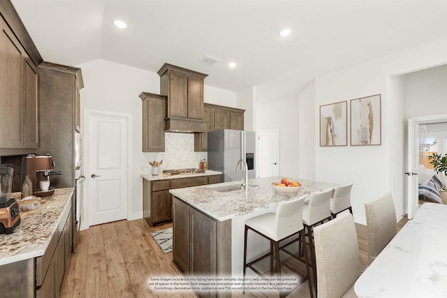 kitchen featuring sink, appliances with stainless steel finishes, a kitchen island with sink, light stone counters, and decorative backsplash