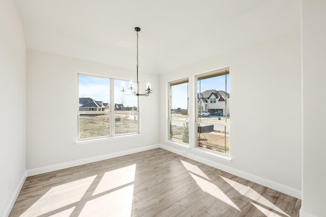 unfurnished dining area with an inviting chandelier, light hardwood / wood-style floors, and a wealth of natural light