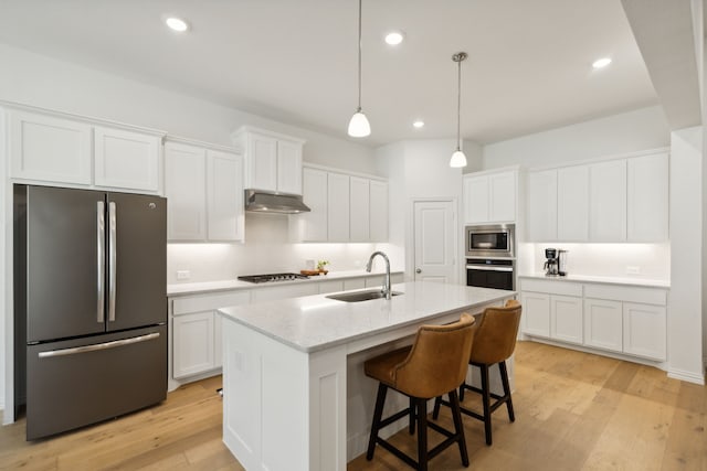 kitchen with appliances with stainless steel finishes, sink, white cabinetry, light hardwood / wood-style floors, and a center island with sink