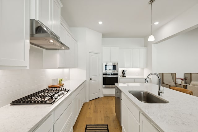 kitchen featuring appliances with stainless steel finishes, extractor fan, light hardwood / wood-style flooring, sink, and decorative light fixtures