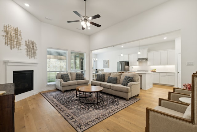 living room featuring light hardwood / wood-style floors, sink, a high ceiling, and ceiling fan