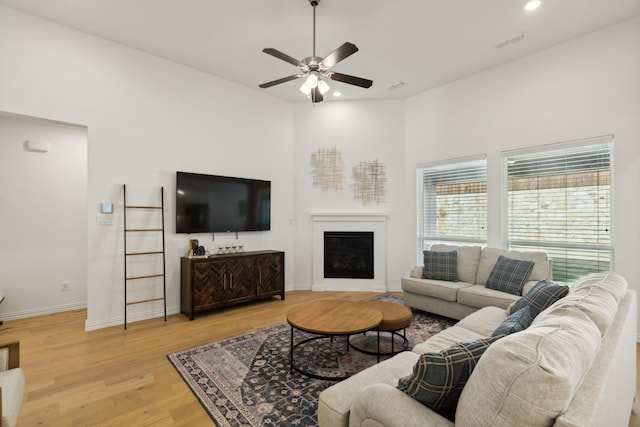 living room with light hardwood / wood-style flooring, a towering ceiling, and ceiling fan