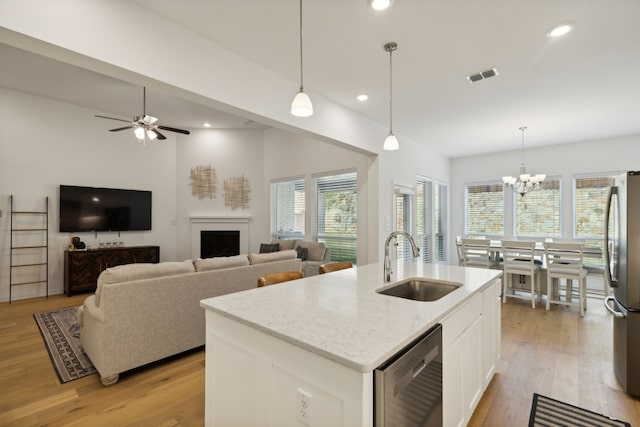 kitchen featuring an island with sink, sink, decorative light fixtures, white cabinets, and light hardwood / wood-style floors