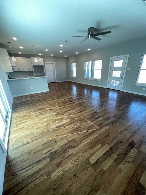 unfurnished living room featuring dark wood-type flooring, plenty of natural light, and ceiling fan