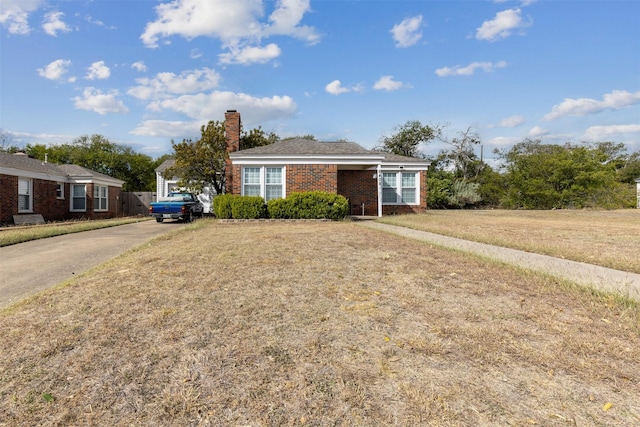 bungalow-style house with brick siding, driveway, a chimney, and a front yard
