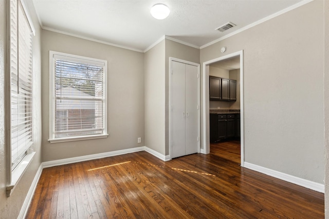 empty room with crown molding, dark wood-style flooring, baseboards, and visible vents
