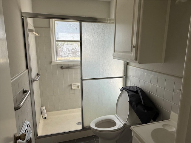 bathroom featuring tile patterned floors, toilet, vanity, a shower with shower door, and tile walls