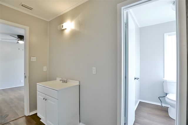 bathroom with toilet, ornamental molding, hardwood / wood-style floors, vanity, and ceiling fan