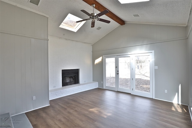 unfurnished living room featuring french doors, vaulted ceiling with skylight, dark hardwood / wood-style flooring, a fireplace, and ceiling fan