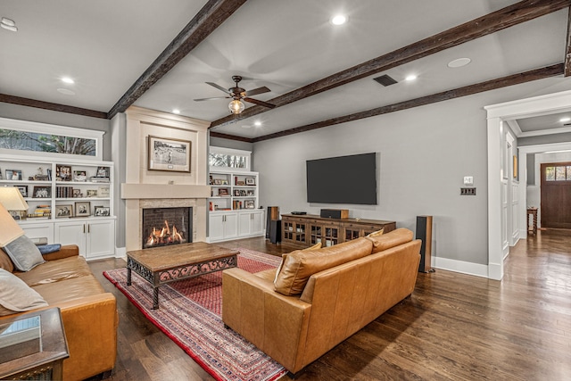 living room with ceiling fan, dark hardwood / wood-style flooring, beamed ceiling, a fireplace, and crown molding