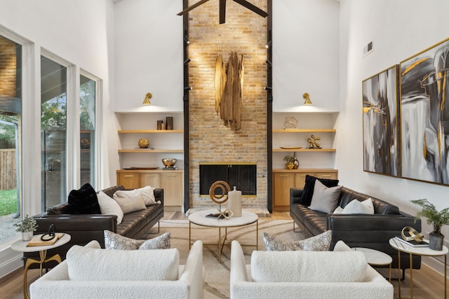 living room featuring built in features, a fireplace, hardwood / wood-style flooring, and a towering ceiling