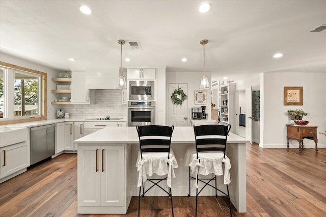 kitchen with backsplash, a kitchen island, hanging light fixtures, stainless steel appliances, and white cabinets