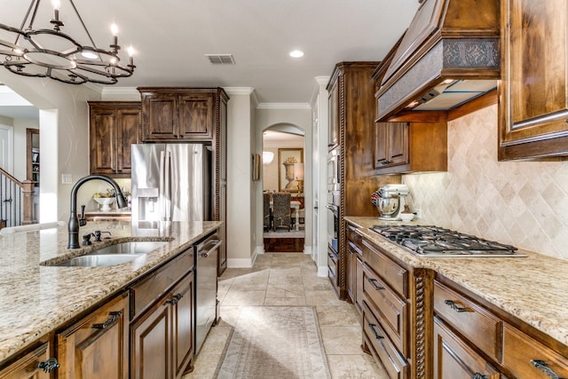 kitchen featuring sink, appliances with stainless steel finishes, light stone countertops, custom exhaust hood, and hanging light fixtures