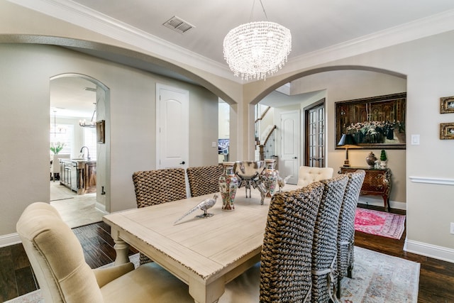 dining room with sink, a chandelier, wood-type flooring, and crown molding