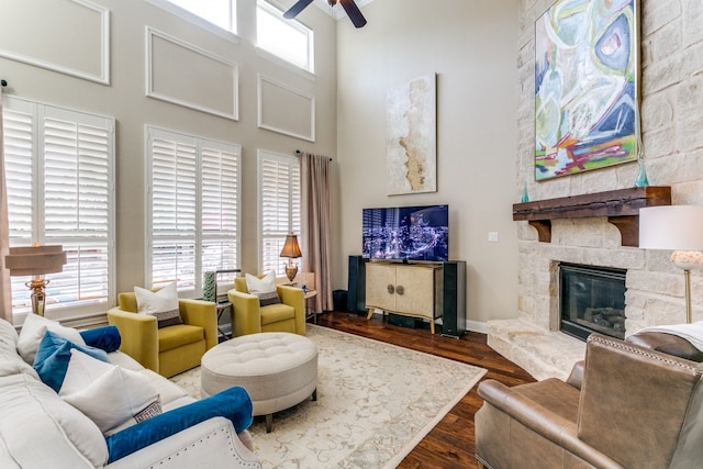 living room with a wealth of natural light, ceiling fan, a stone fireplace, and dark hardwood / wood-style flooring