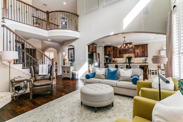 living room featuring dark wood-type flooring, a healthy amount of sunlight, a high ceiling, and a notable chandelier