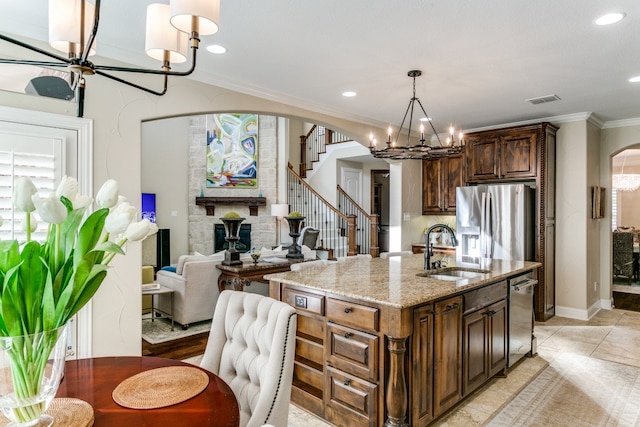 kitchen with light stone counters, ornamental molding, a center island with sink, stainless steel appliances, and sink