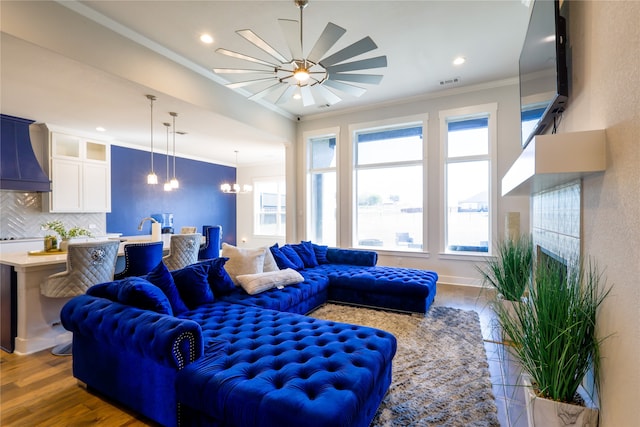 living room with hardwood / wood-style floors, crown molding, and ceiling fan with notable chandelier