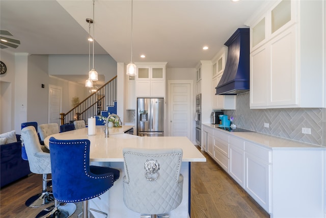 kitchen with a kitchen island with sink, dark wood-type flooring, hanging light fixtures, custom range hood, and stainless steel appliances