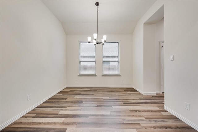 unfurnished room with lofted ceiling, a chandelier, and light wood-type flooring