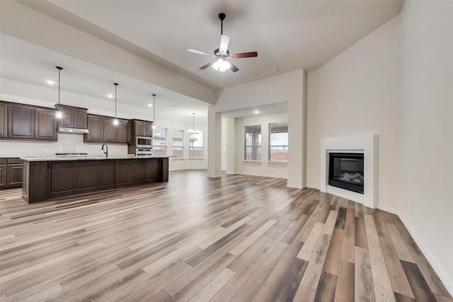 unfurnished living room featuring sink, ceiling fan with notable chandelier, and light hardwood / wood-style flooring