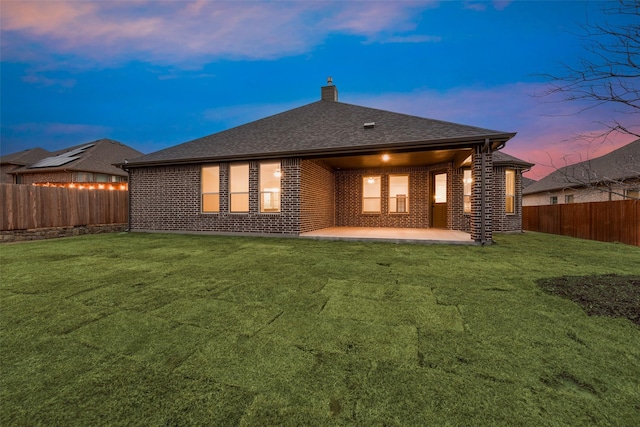 back house at dusk featuring a patio and a lawn