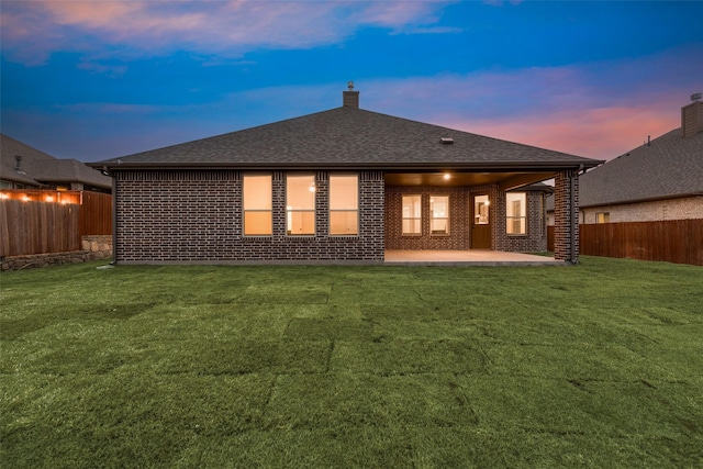 back house at dusk featuring a patio area and a lawn