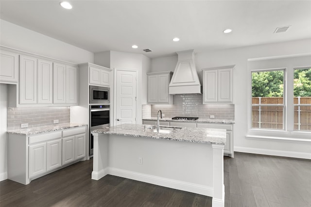 kitchen featuring appliances with stainless steel finishes, custom exhaust hood, white cabinets, and a kitchen island with sink