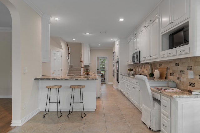 kitchen featuring kitchen peninsula, backsplash, white cabinetry, light stone countertops, and stainless steel appliances