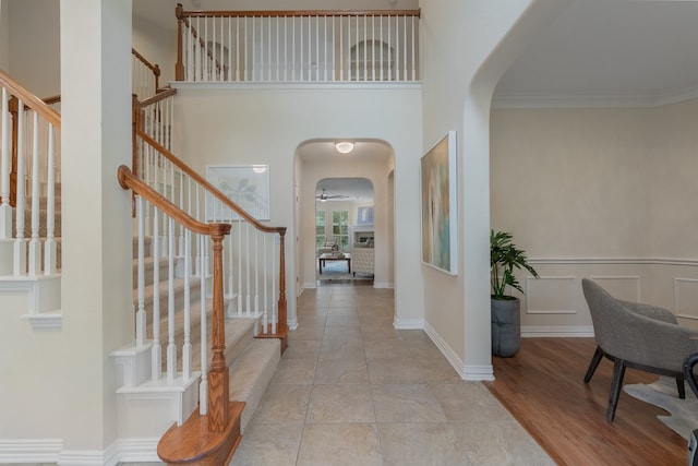 foyer entrance featuring a towering ceiling, ornamental molding, light wood-type flooring, and ceiling fan