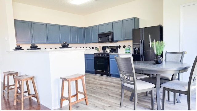 kitchen with a breakfast bar area, kitchen peninsula, black appliances, blue cabinetry, and light hardwood / wood-style floors