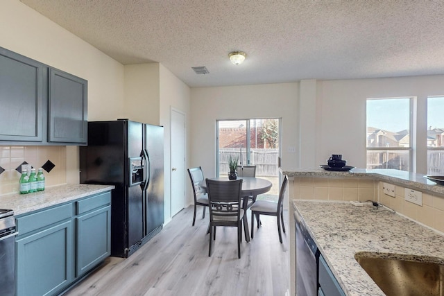 kitchen with tasteful backsplash, a textured ceiling, light stone countertops, light hardwood / wood-style floors, and stainless steel appliances