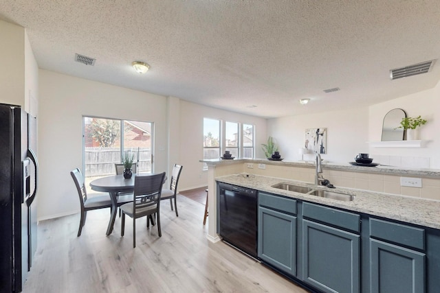 kitchen featuring light stone countertops, black appliances, sink, light wood-type flooring, and a textured ceiling