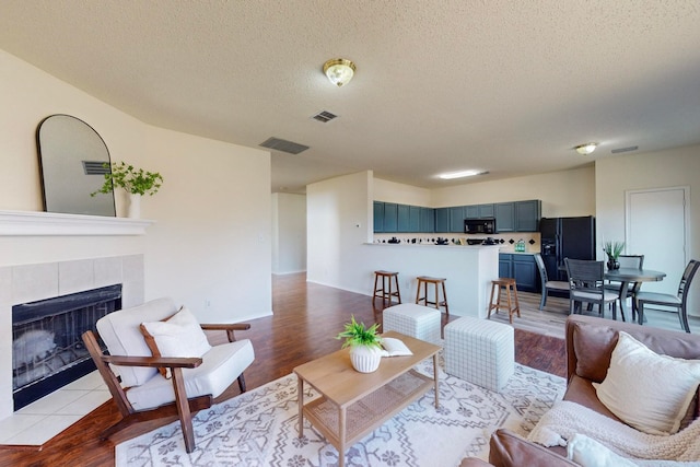 living room with light hardwood / wood-style floors, a textured ceiling, and a tile fireplace