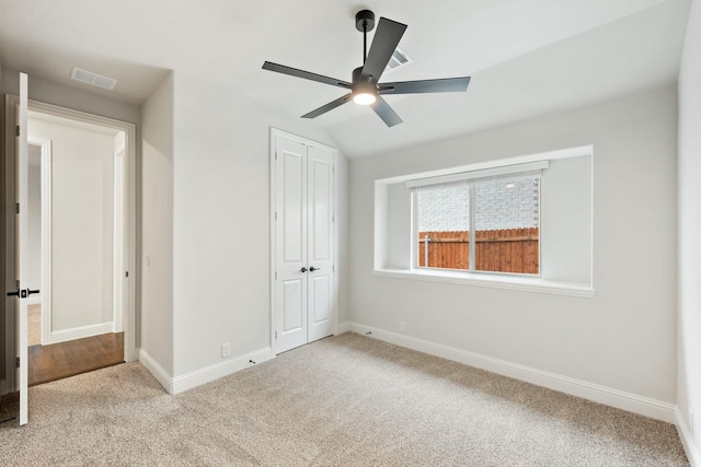 unfurnished bedroom with lofted ceiling, a closet, visible vents, carpet flooring, and baseboards