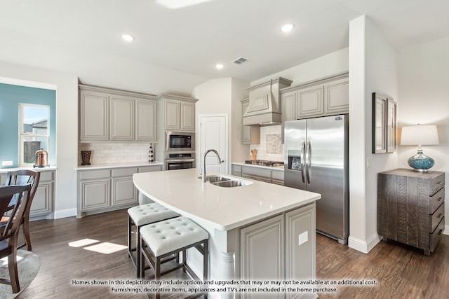 kitchen with an island with sink, custom range hood, stainless steel appliances, sink, and dark hardwood / wood-style flooring