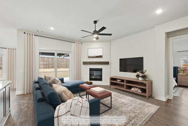 living area with visible vents, a large fireplace, ceiling fan, a textured ceiling, and wood finished floors