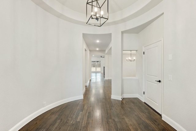 hallway with a notable chandelier, dark wood finished floors, and baseboards