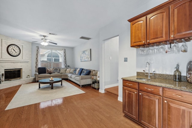 living room with indoor wet bar, a fireplace, light hardwood / wood-style floors, and ceiling fan