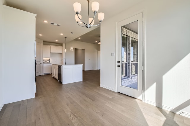 kitchen featuring light wood-type flooring, sink, white cabinetry, hanging light fixtures, and an island with sink