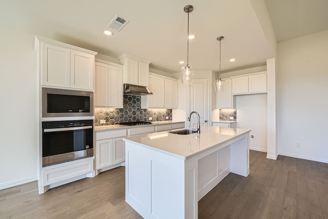 kitchen with a kitchen island with sink, white cabinets, sink, light hardwood / wood-style flooring, and stainless steel appliances