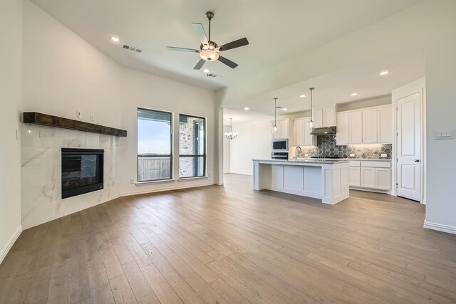 kitchen featuring stainless steel appliances, a center island with sink, white cabinets, light hardwood / wood-style floors, and hanging light fixtures