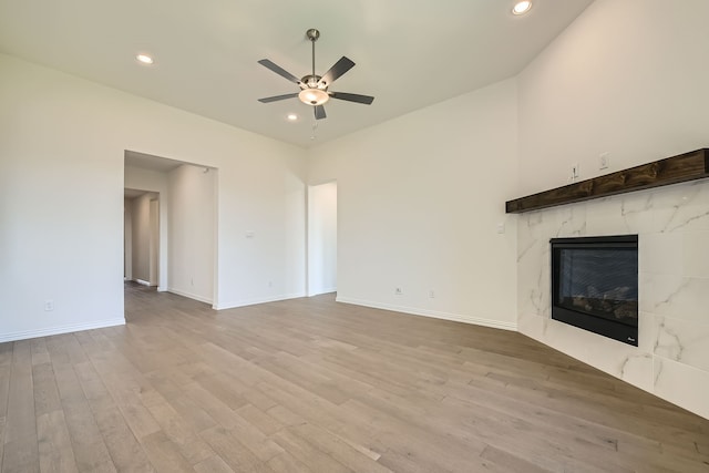 unfurnished living room with a high end fireplace, light wood-type flooring, and ceiling fan