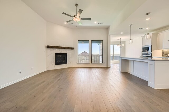 unfurnished living room with ceiling fan with notable chandelier, light wood-type flooring, sink, and a high end fireplace